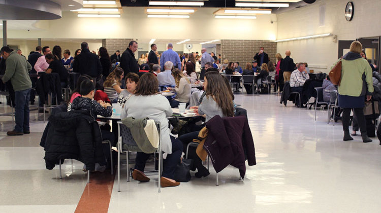 Families of athletes sit at a table and socialize. After eating, they headed to the auditorium for the ceremony.