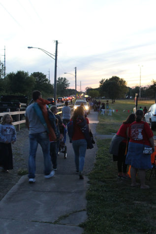 A large crowd files down the sidewalk and cars back up the street. The park was very crowded.