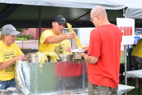  A man receives a husk of corn. The corn that was offered at the roast was either buttered or unbuttered. 